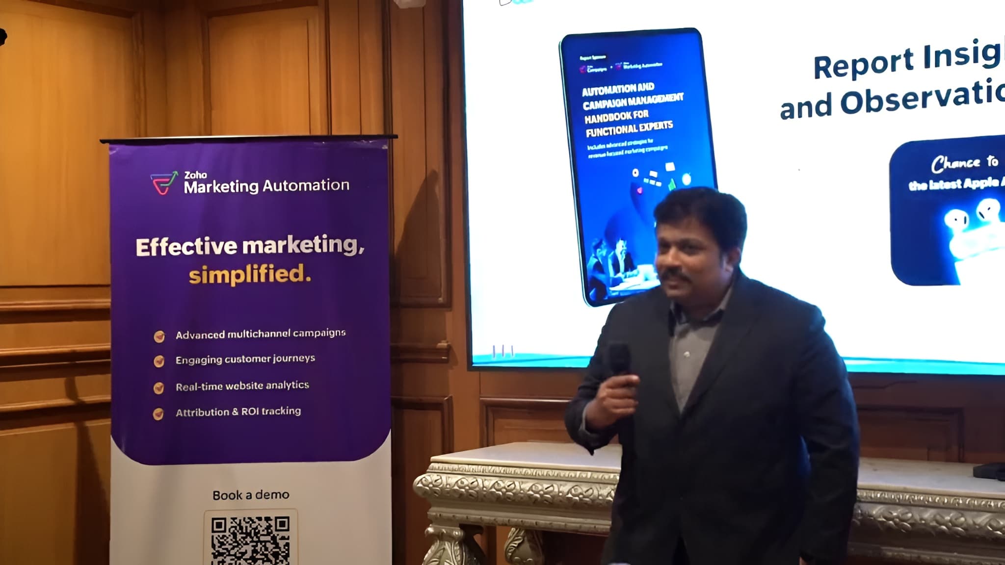 A speaker presenting the Automation and Campaign Management Handbook, its cover on the screen behind him